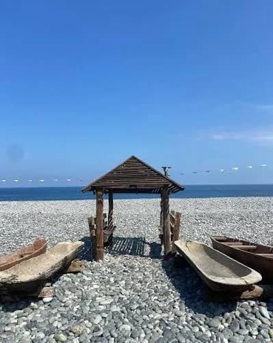 A bamboo hut and stone boats on the grey pebble shore of Luna's Pebble Beach.
